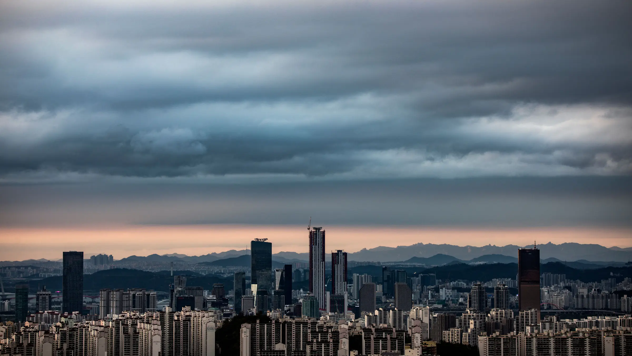 Seoul business district skyline at dusk, high-rise towers backed by mountain ridges