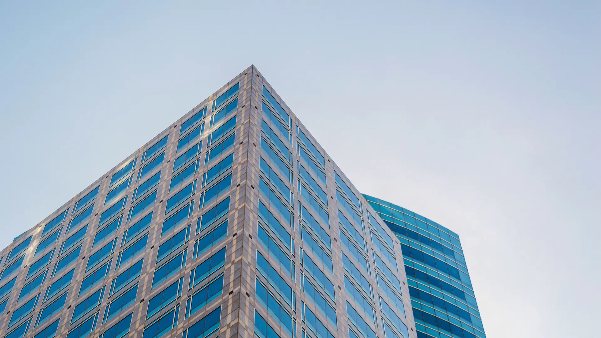 Glass-clad corporate office tower seen from street level against an open sky